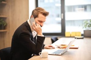 Man talks on phone and looks at laptop